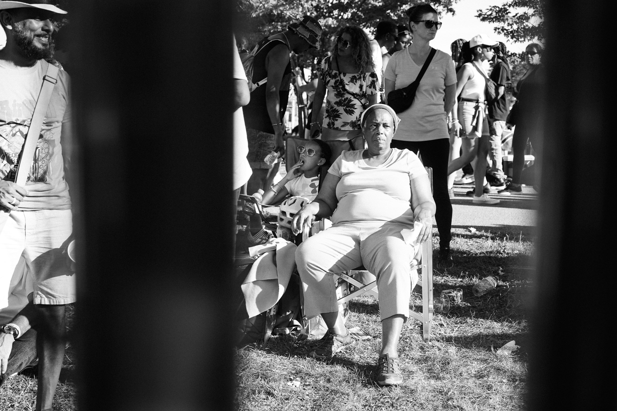 Grandmother seated with a child on her lap at an outdoor event, seen through a fence